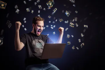 A man celebrating a winning moment on his laptop while gaming symbols float around him, capturing the excitement of 2777BED games.